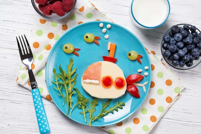 Funny sandwich with cheese in a shape of submarine and fishes, meal for kids idea, top view on wooden background